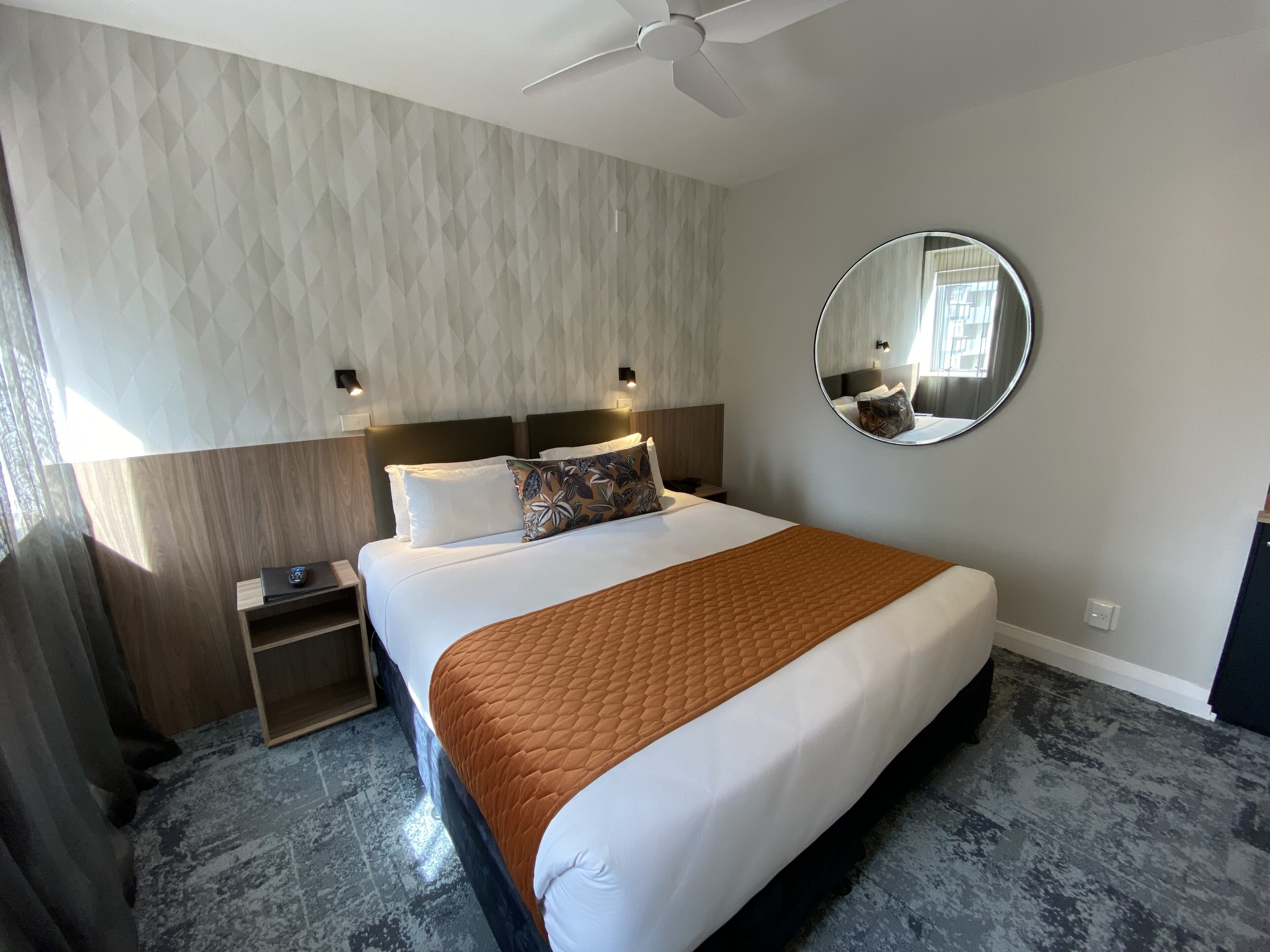 Una habitación de hotel moderna con una cama grande, un espejo redondo y un ventilador de techo.