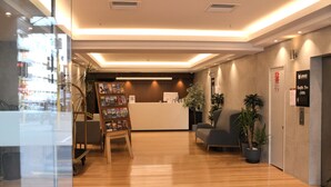 Zona de recepción con suelo de madera, un mostrador, un área de estar con sofá y una estantería.