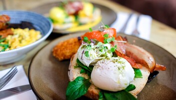A breakfast setting with a plate of eggs benedict, bacon, and greens.