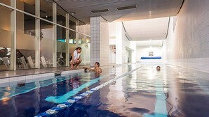 Una piscina interior con carriles delimitados, pared de azulejos y una partición de cristal que refleja a una persona.