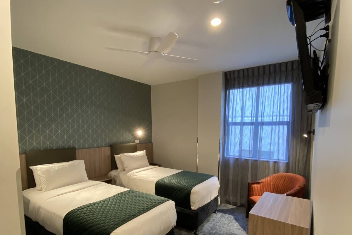Ein Hotelzimmer mit zwei Betten, einem Deckenventilator, einem Fernseher und einem Fenster mit Vorhängen.