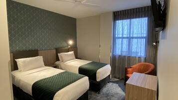 Ein Hotelzimmer mit zwei Betten, einem Deckenventilator, einem Fernseher und einem Fenster mit Vorhängen.