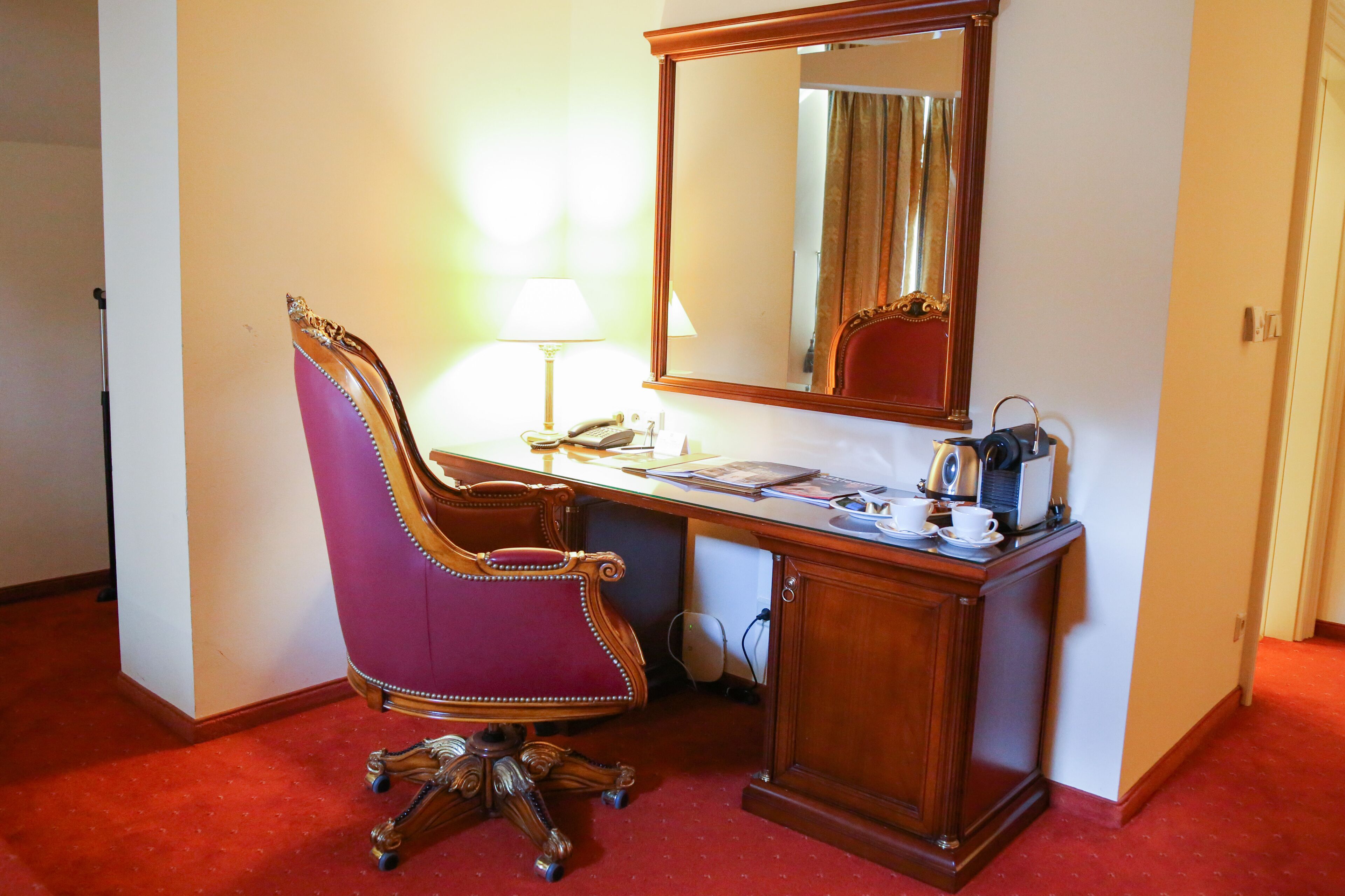A room with a wooden desk, a purple chair, a mirror, a lamp, and a telephone.