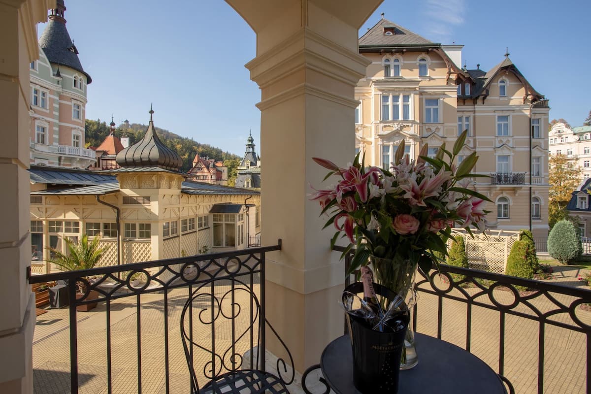Uma varanda com vista para edifícios históricos, um vaso de flores e guarda-corrimão de metal.