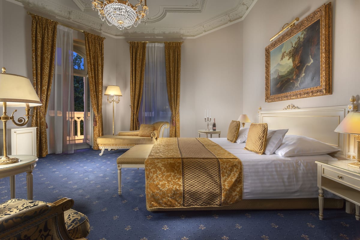 Um quarto luxuoso com uma cama grande, um chaise longue e um candelabro.