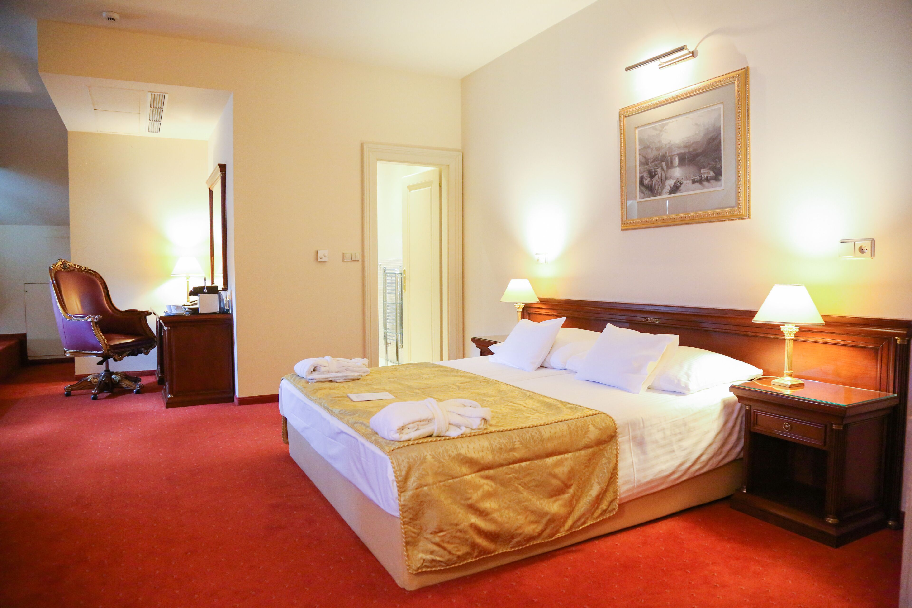 Une chambre d’hôtel avec un grand lit, une table de chevet en bois, un bureau avec une chaise et un tableau encadré au mur.