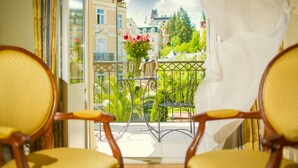 Een balkon met twee houten stoelen, een metalen tafel en een bloevas.
