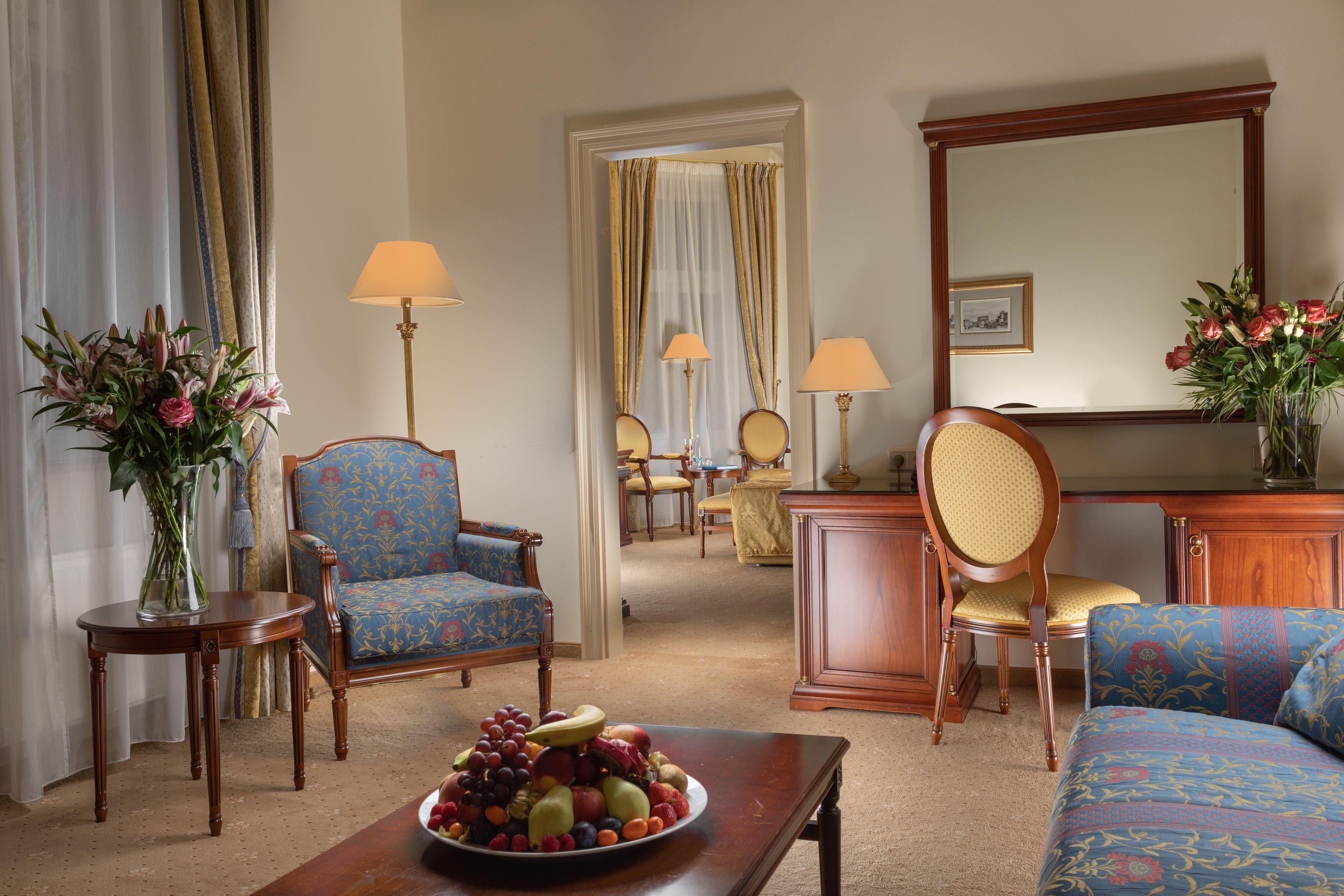 A hotel room with a dining area, a sofa, a table with fruit, and a mirror.