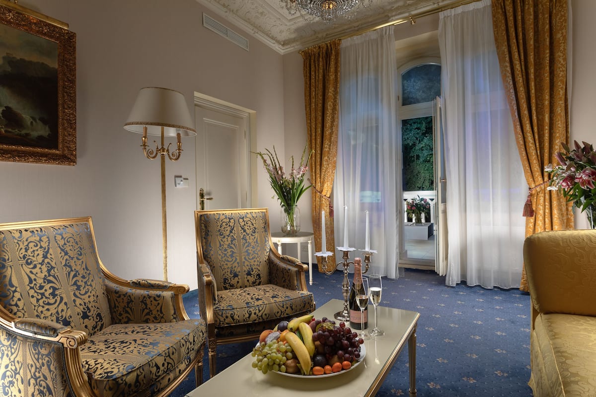Quarto luxuoso com mobiliário requintado, uma cesta de frutas e vista para uma varanda.