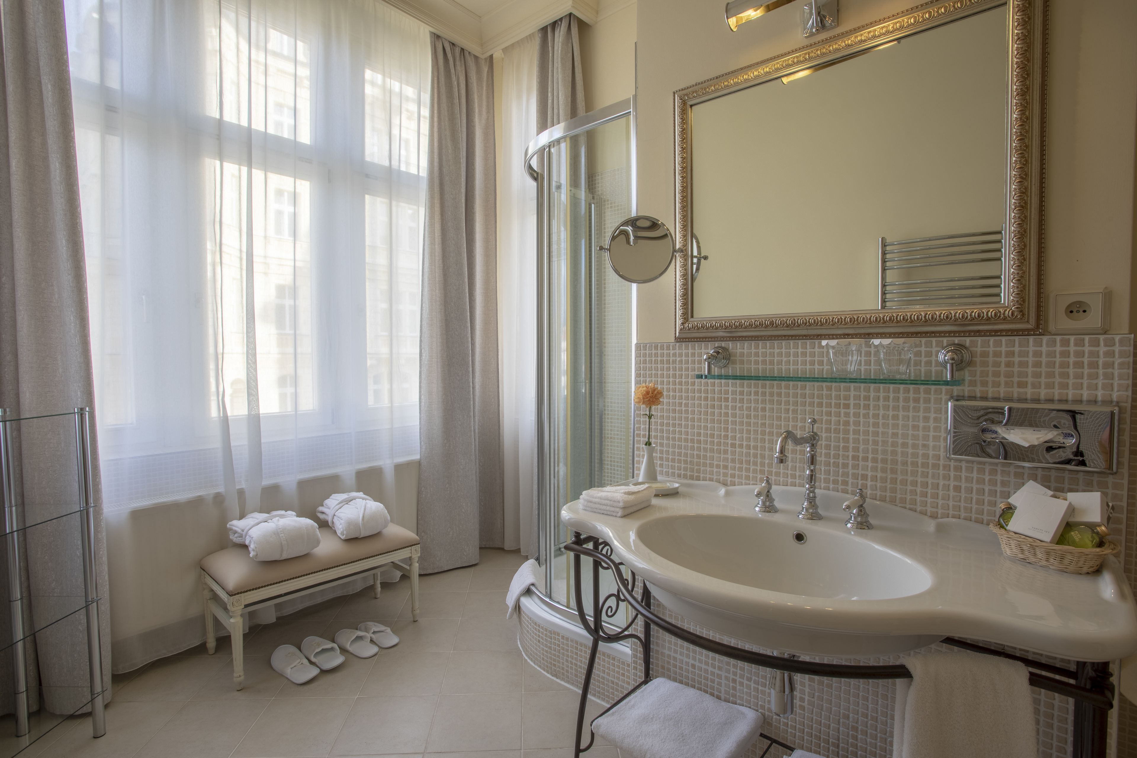 Un baño con un lavamanos grande, un espejo, un banco con toallas y una zona de ducha.