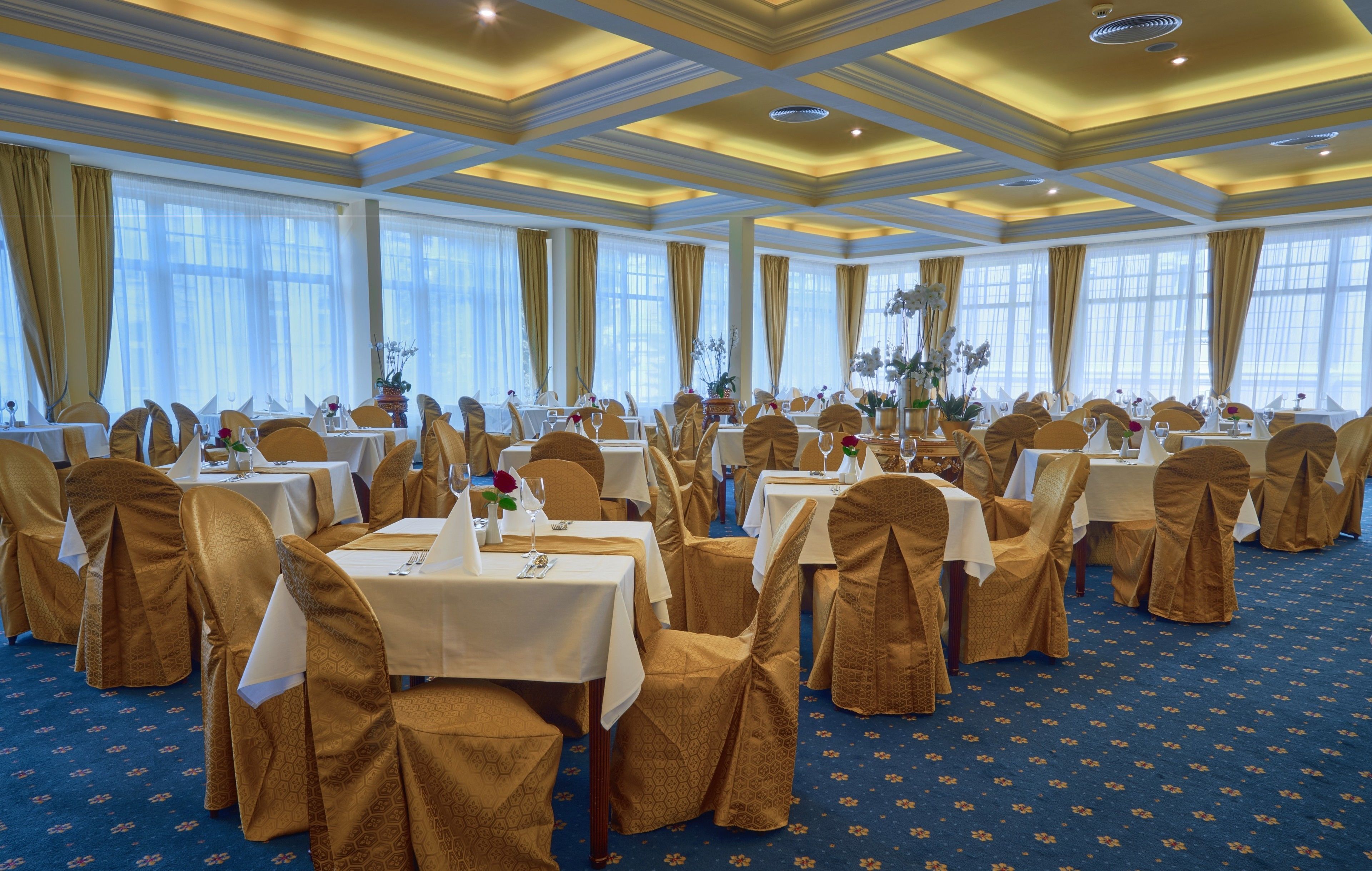 A banquet hall with round tables, chairs, and floral centerpieces.
