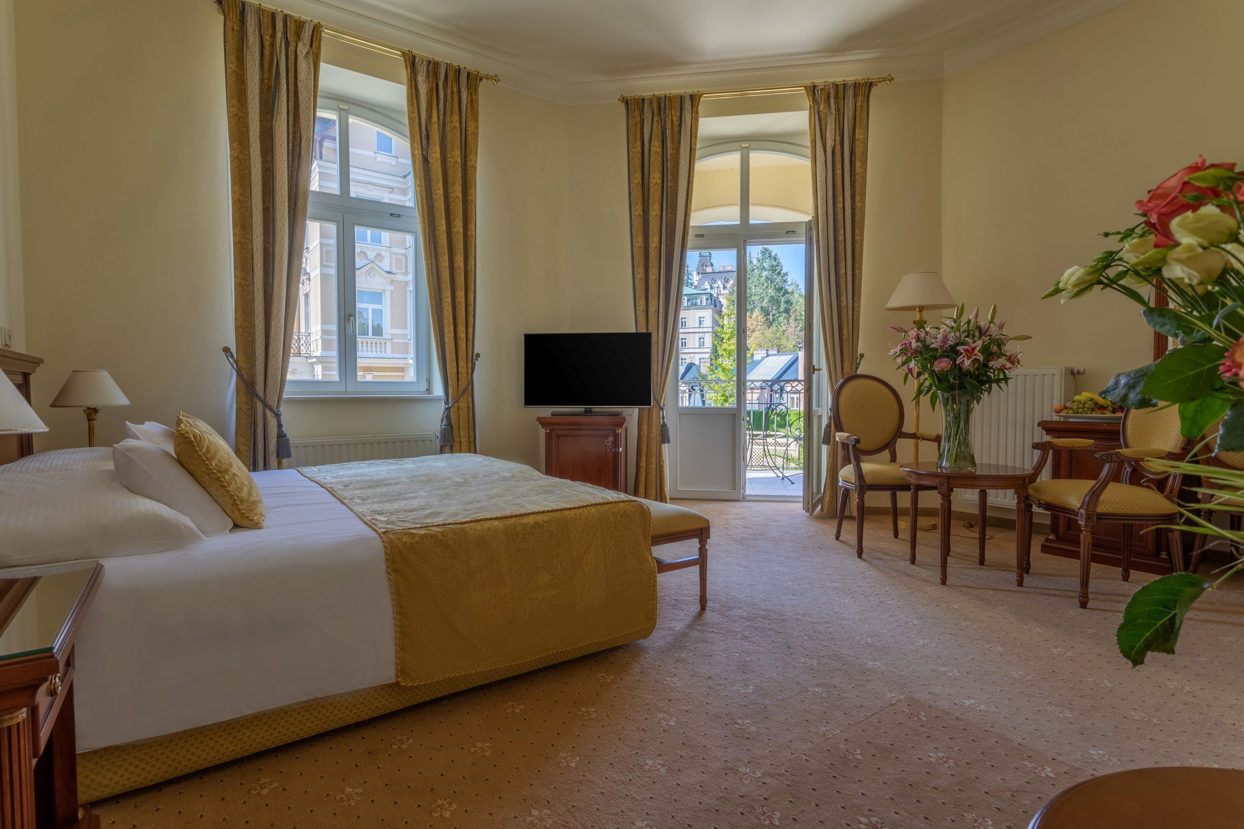 A hotel room with a bed, a television, a desk with a chair, and a view of buildings through the window.