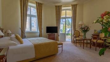 A hotel room with a bed, a television, a desk with a chair, and a view of buildings through the window.