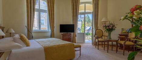 Habitación de hotel con cama, televisor, escritorio con silla y vista a edificios a través de la ventana.