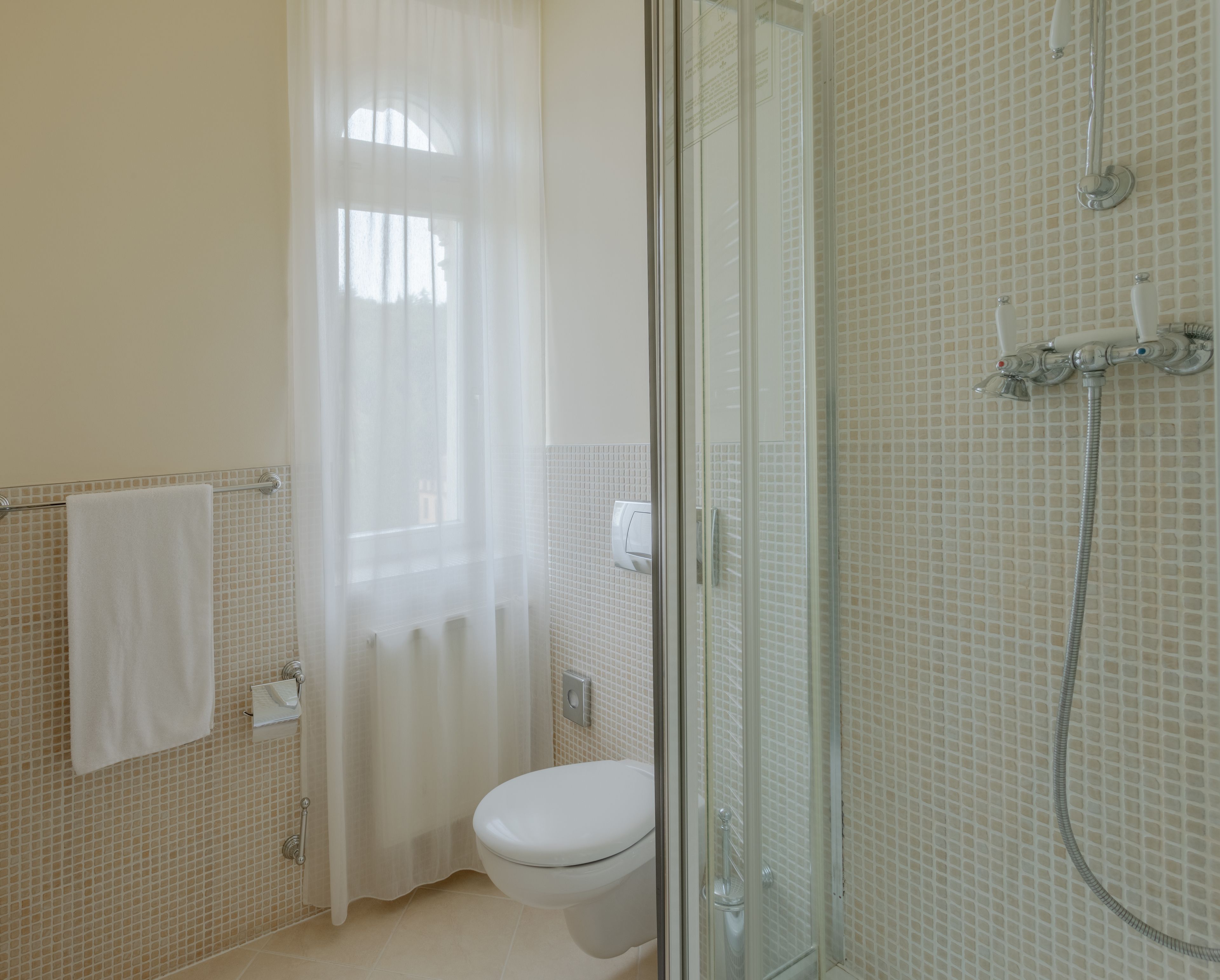Un baño con inodoro, cabina de ducha de vidrio y cortina blanca.