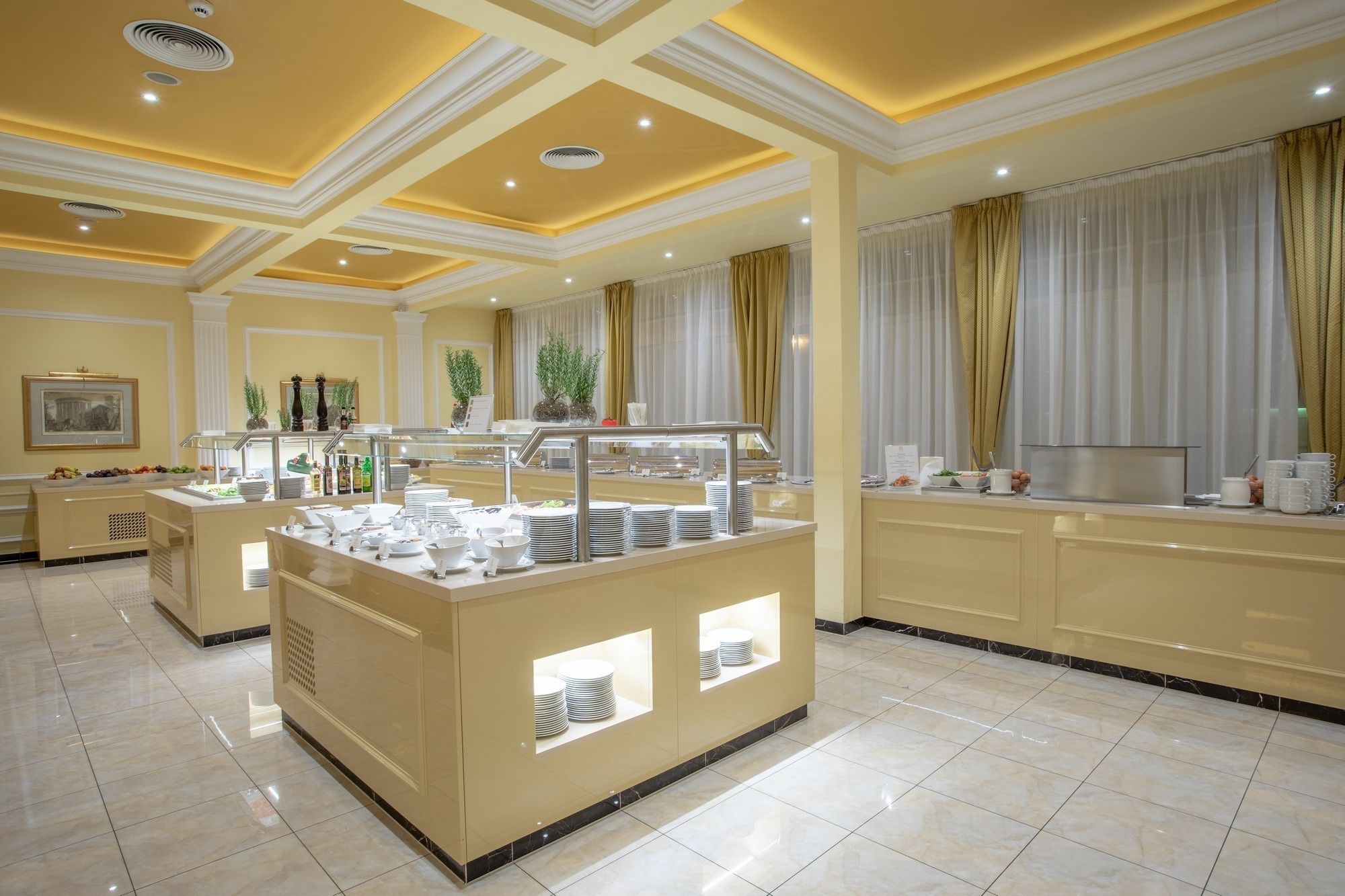 Zona de desayuno de hotel con barra de buffet, que ofrece una variedad de alimentos y bebidas.