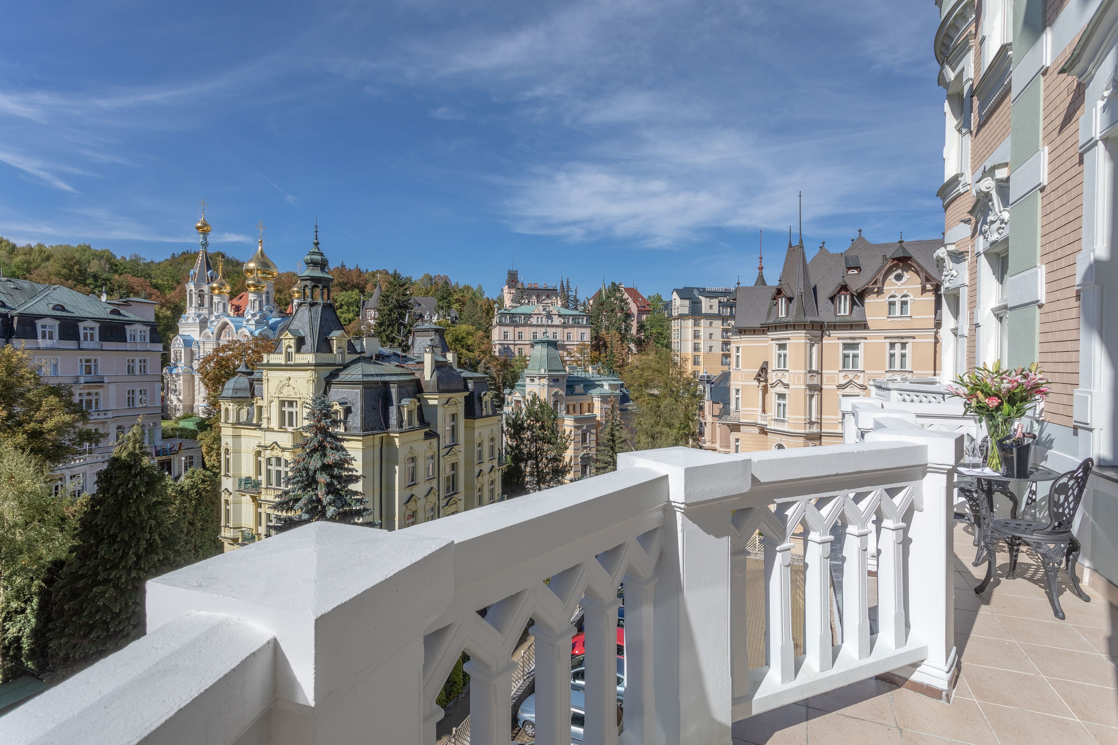 A balcony with a white balustrade overlooking a cityscape with historic buildings and a church with golden domes.