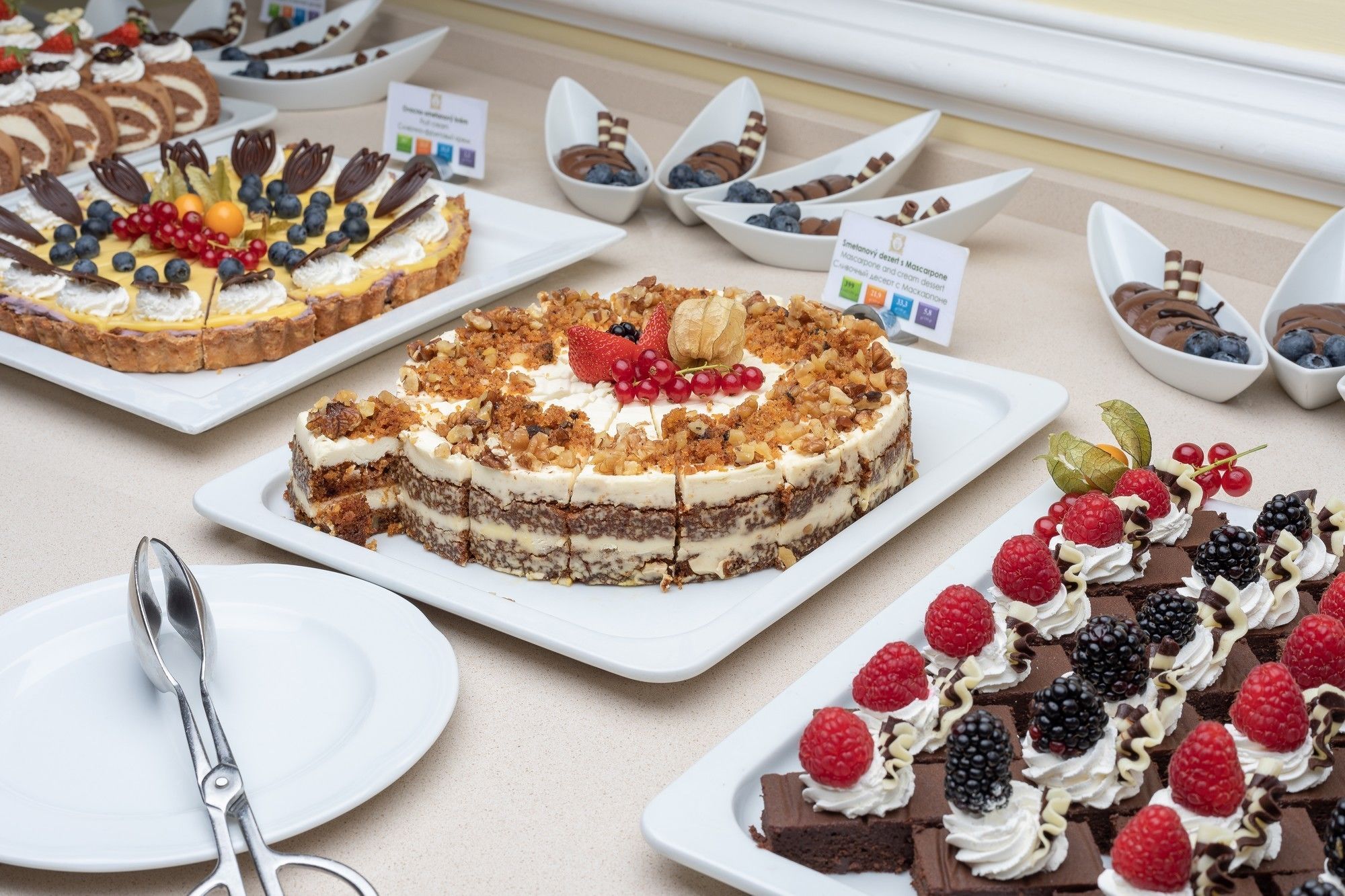 A variety of desserts on display, including cakes with fruit toppings and a selection of chocolate desserts in small bowls.