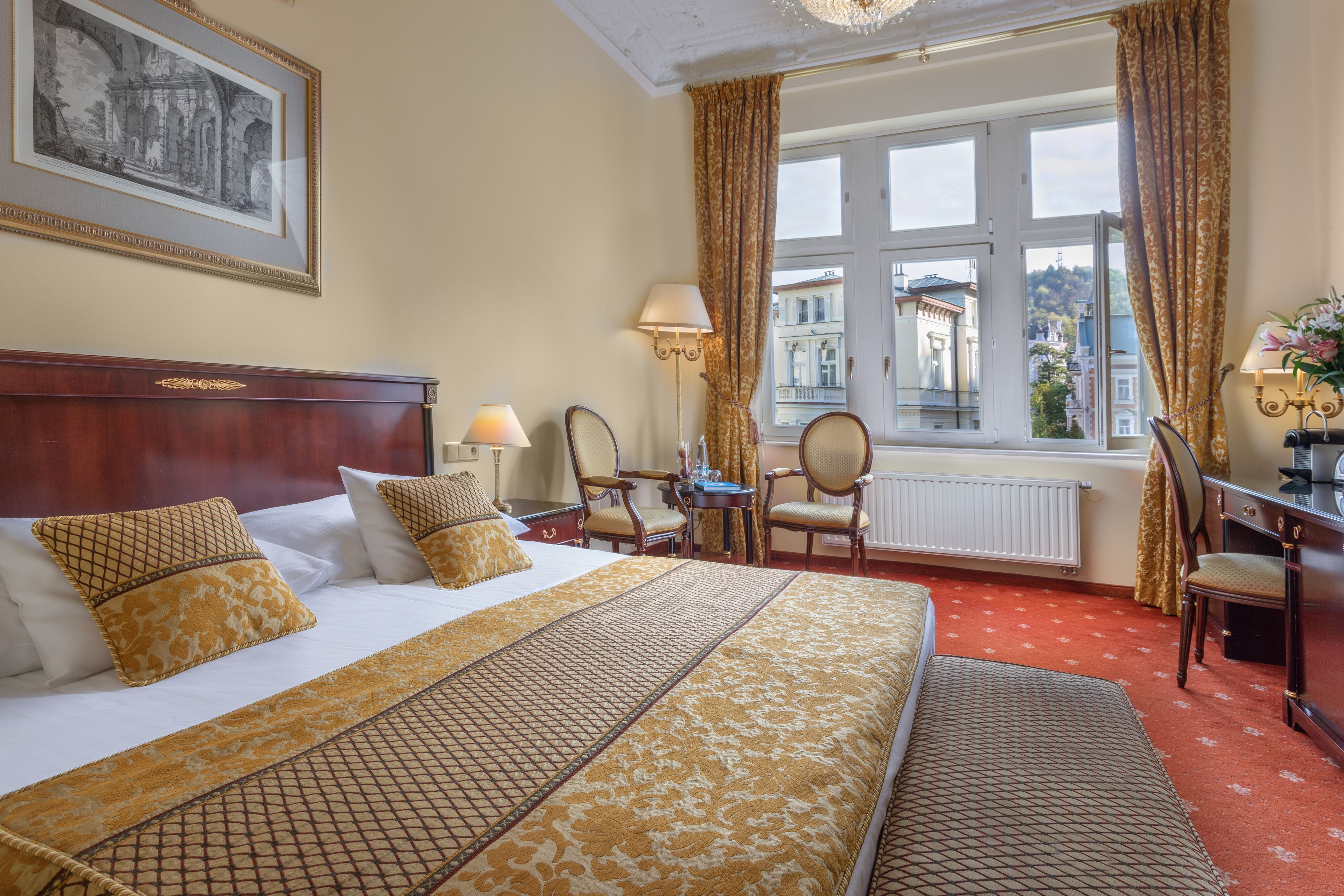 A hotel room with a large bed, a desk, and a view of buildings through the window.