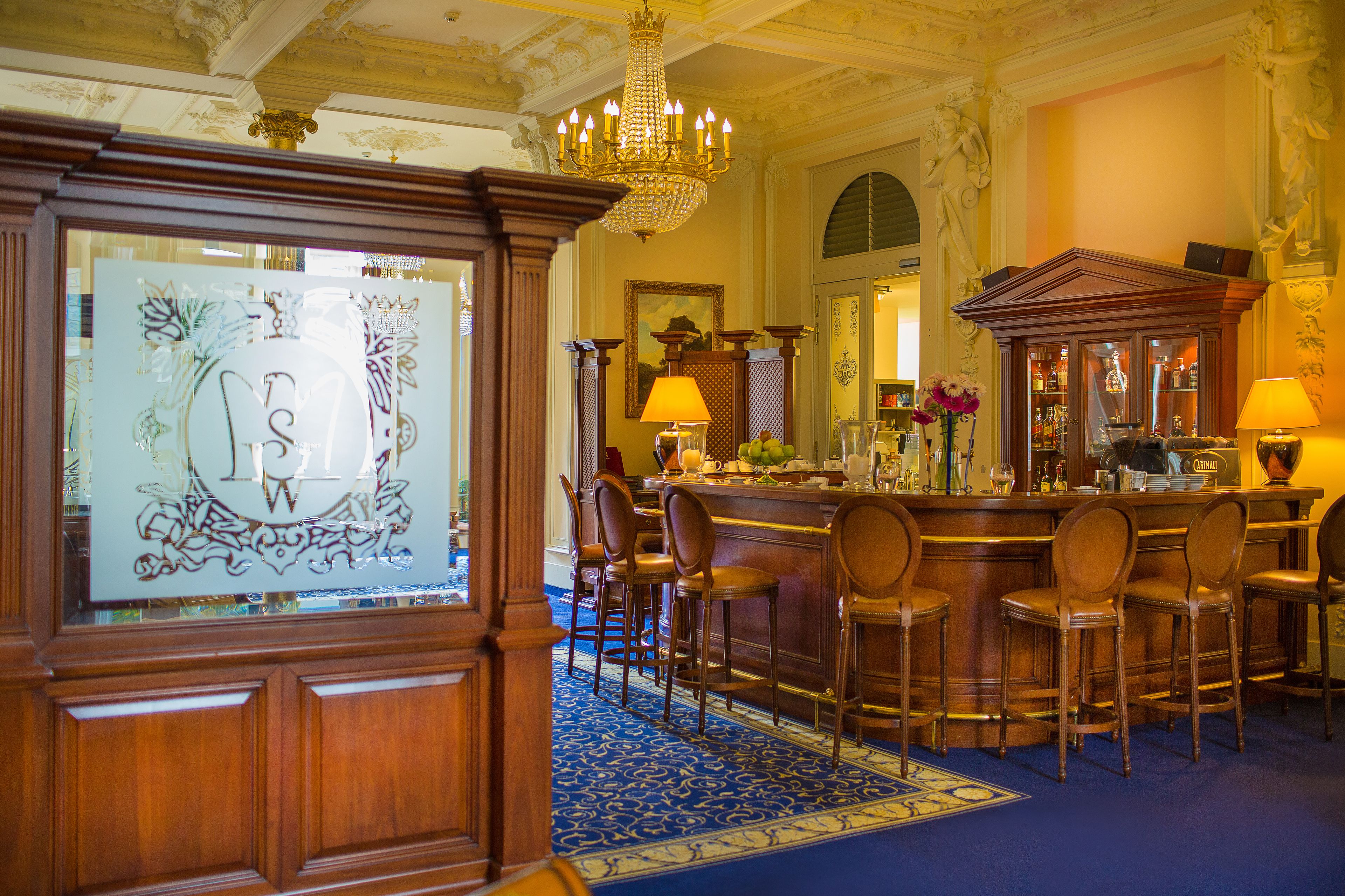 A bar area with a chandelier, bar stools, and a decorative mirror.