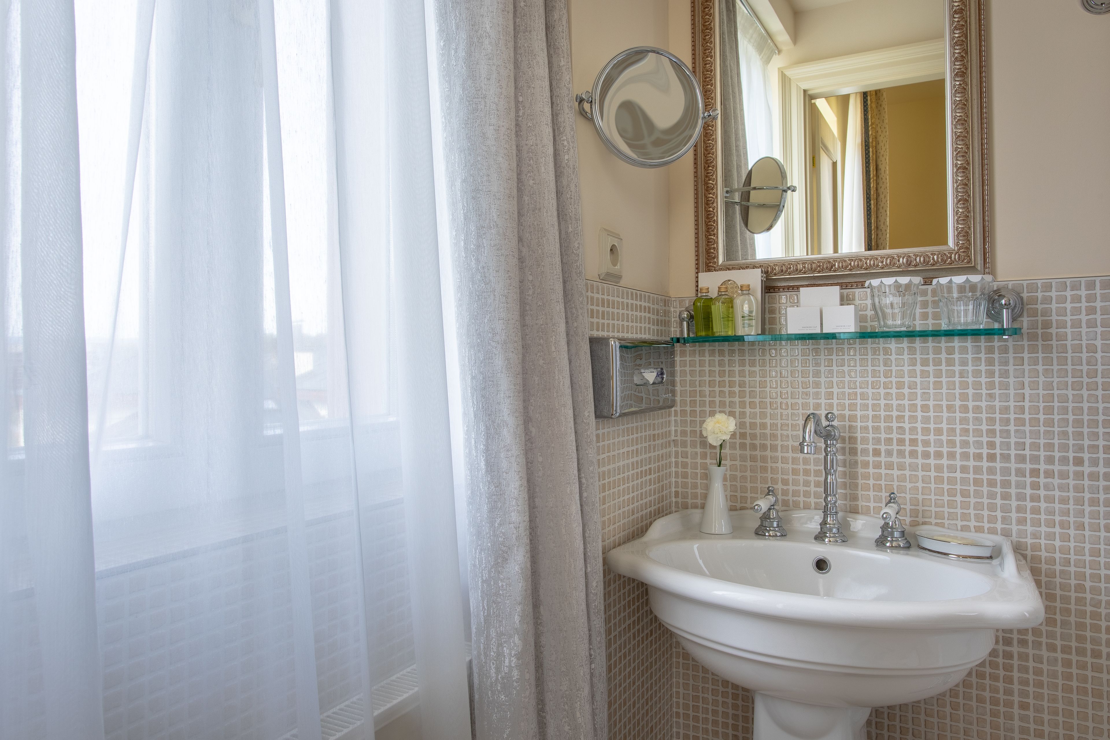 A bathroom with a white sink, a mirror, and a glass shelf above it.