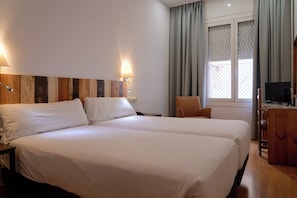 A hotel room with two beds, a desk, a chair, a TV, and a window with curtains. - Hotel Miramar Badalona (Badalona)