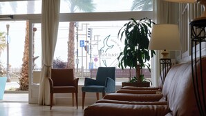 Een hotel lobby met een zithoek, een grote plant en uitzicht op de straat.