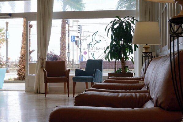 A hotel lobby with a seating area, a large plant, and a view of the street outside.