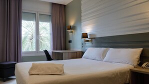 Een hotelkamer met een bed, nachtkastje, lamp en raam met gordijnen.