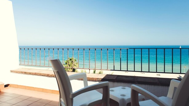Een balkon met uitzicht op de oceaan, witte stoelen en een tafel.