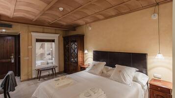 A hotel room with a large bed, a wooden wardrobe, a small table, and a chair.