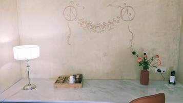 Un escritorio con una lámpara, un jarrón con flores, una caja con objetos y un diseño decorativo en la pared.