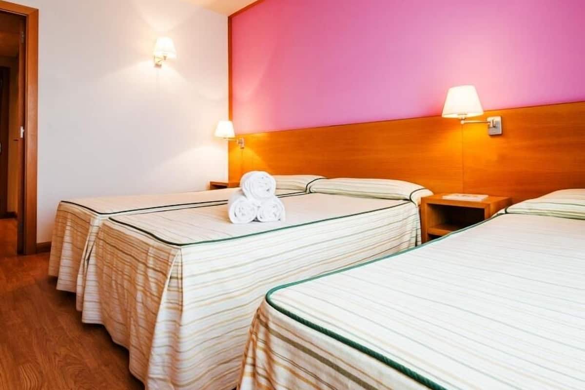 Habitación de hotel con tres camas, cada una con cubrecama a rayas y cabecero de madera. Hay dos lámparas de pared a cada lado de las camas.