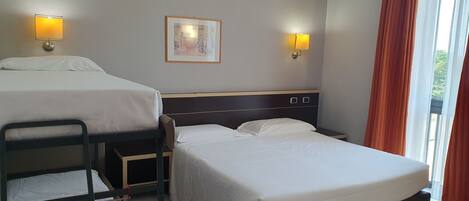A hotel room with two beds, a small table, and a chair. There are two wall-mounted lamps and a framed picture on the wall.