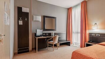 A hotel room with a desk, chair, bed, and a large window with curtains.