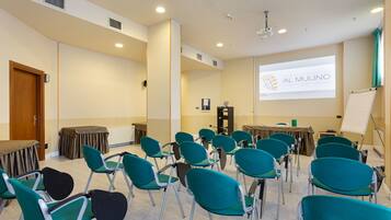 Une salle de conférence avec des chaises de couleur turquoise, un écran de projection affichant le texte « AL MULINO », et un tableau blanc.