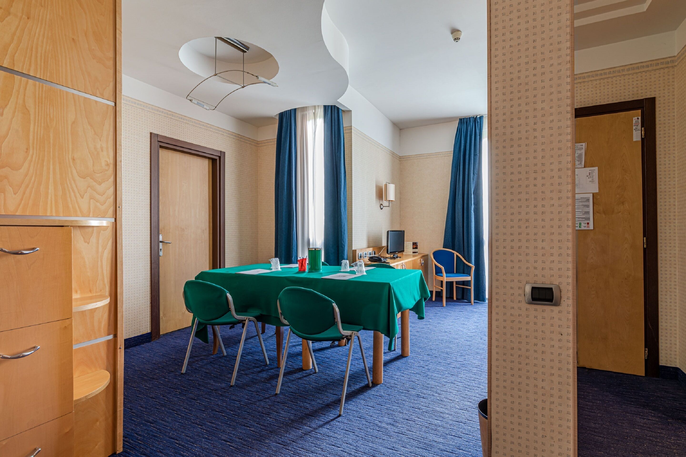 A hotel room with a conference table, chairs, a desk with a computer, and a TV.