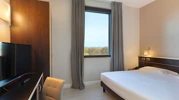 Una habitación de hotel con cama, televisión, escritorio y ventana con cortinas.