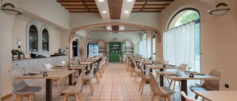Un restaurante espacioso con techos altos, arcos de ladrillo en forma de arco y un mostrador verde central. Las mesas están dispuestas en filas con sillas.