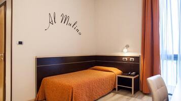 A hotel room with a bed, a bedside table with a lamp, a chair, and a wall with the name "Al Mulino".