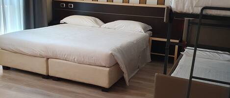 Habitación de hotel con una cama grande, una cama litera, suelo de madera y un diseño de pared a rayas.