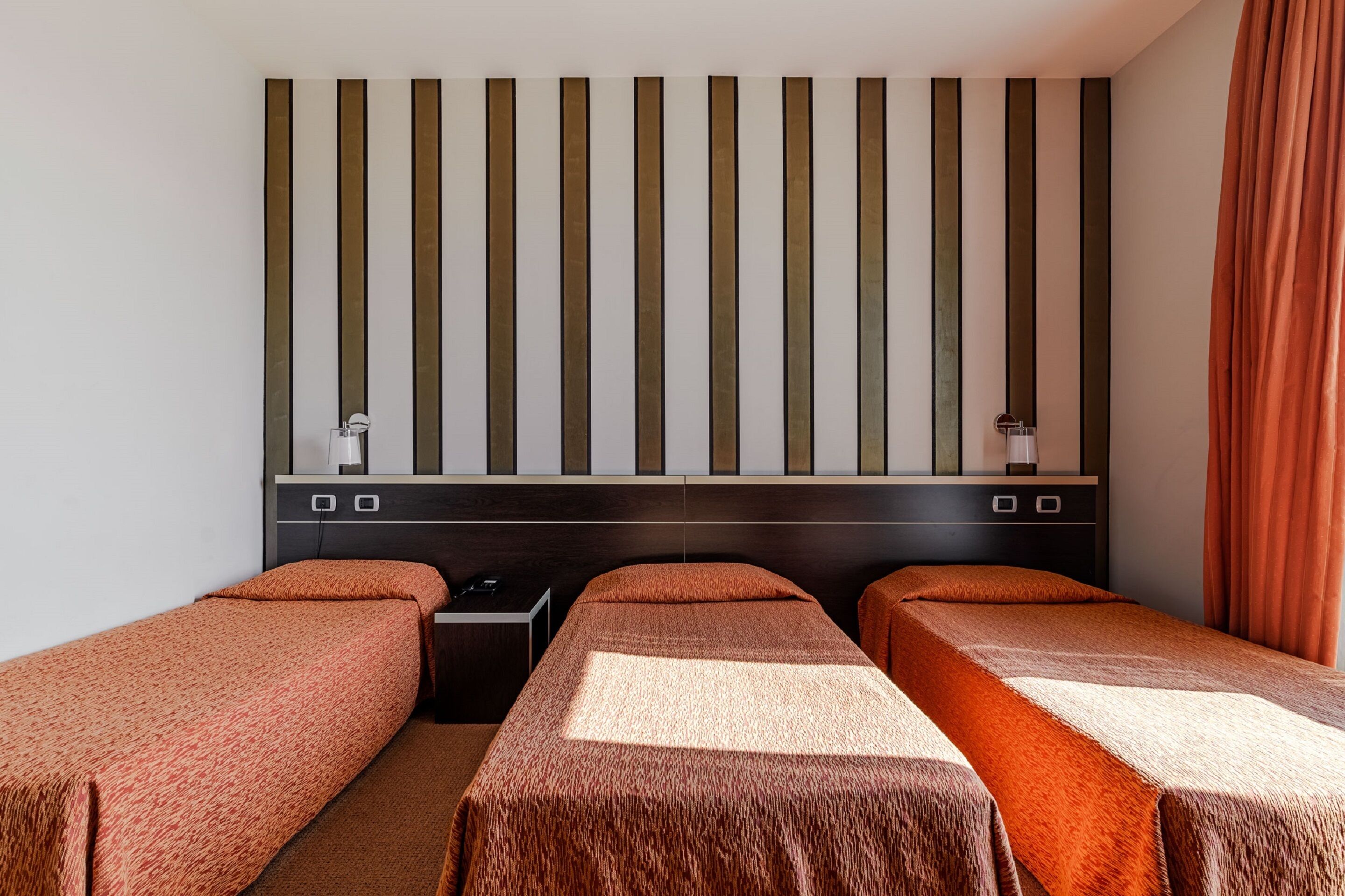 Habitación de hotel con dos camas individuales, cabecera oscura, una mesita pequeña y estante fijado a la pared.