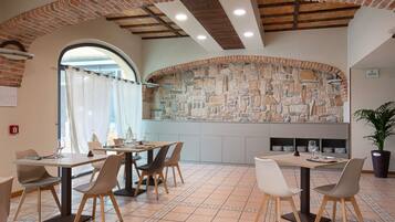 A restaurant with brick arches, stone walls, and tiled flooring. Tables and chairs are arranged for dining.