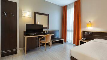 Habitación de hotel con cama, escritorio, silla, televisor y espejo.