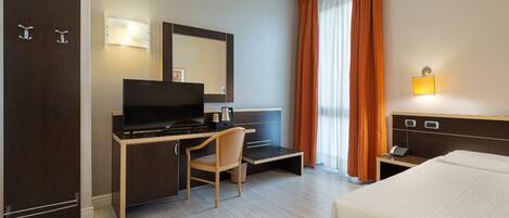 Habitación de hotel con cama, escritorio, silla, televisor y espejo.
