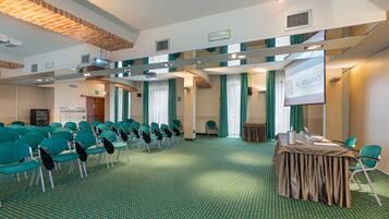 A conference room with rows of teal chairs, a projector screen, and a table with a laptop and papers.