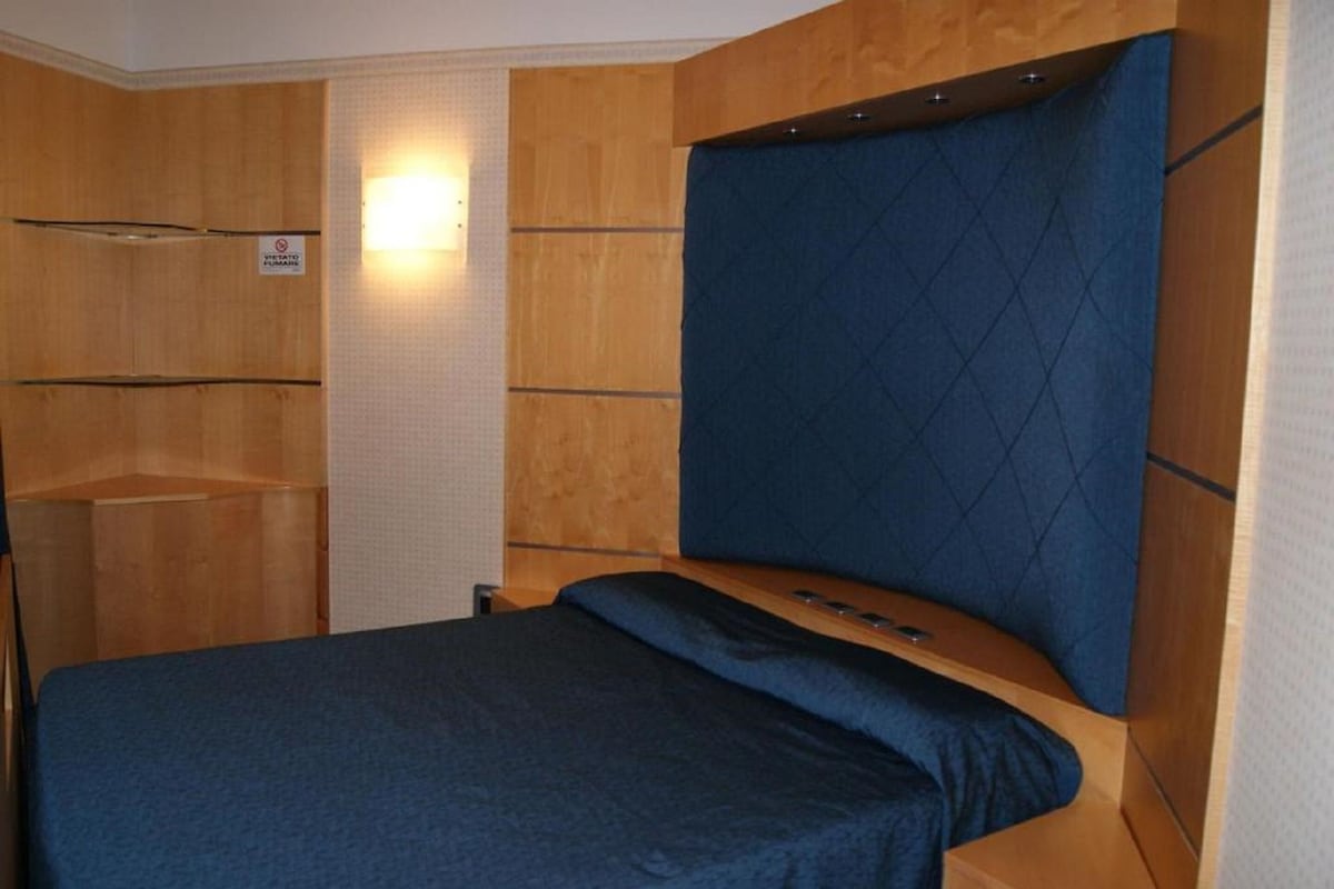 Un dormitorio con cama, cabecera de madera y una pequeña repisa.