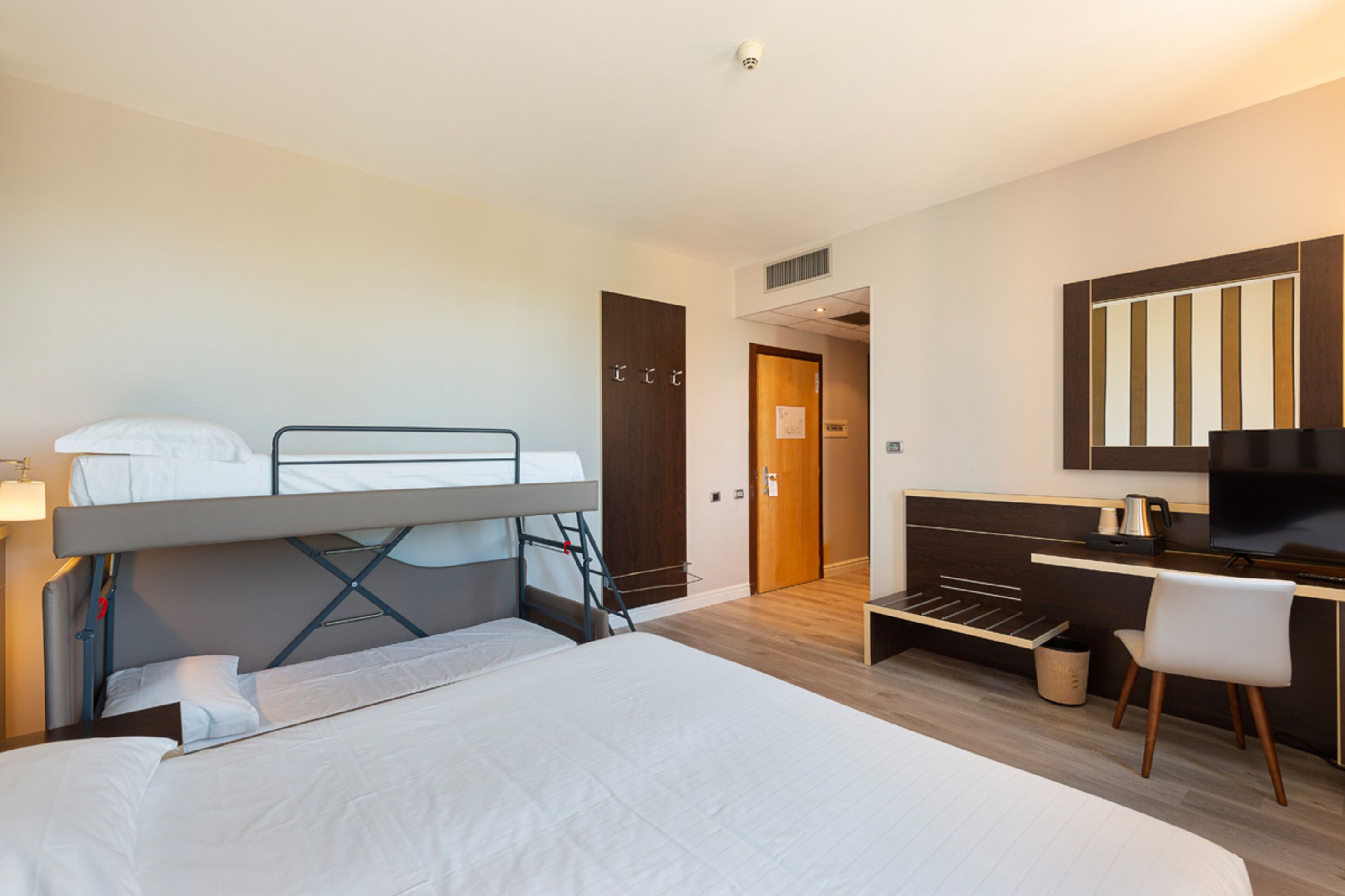A modern hotel room with a bunk bed, a desk, and a television.