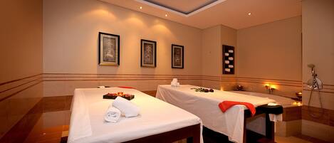 Een spa-ruimte met twee massagetafels, elk met een handdoek en een roos. Er hangen ingelijste foto’s aan de muur en er is een grote spiegel.