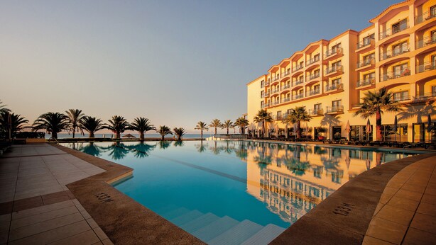 Ein Hotel mit Schwimmbad, Palmen und blauem Himmel.